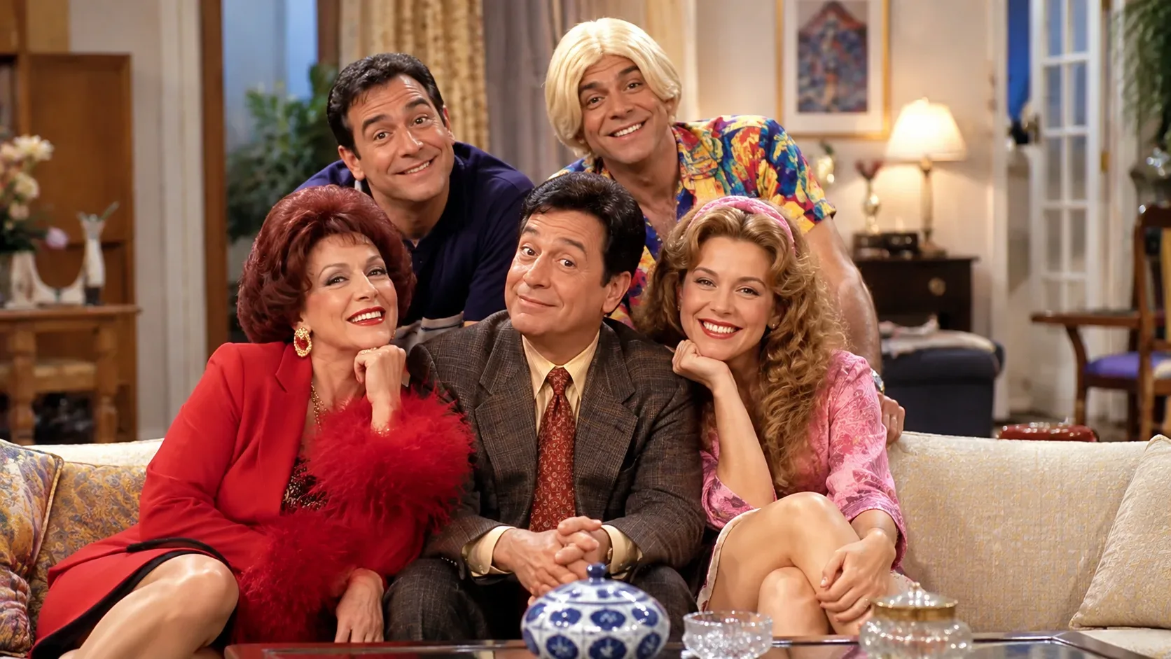 Grupo de cinco personagens em uma sala de estar com estética de sitcom televisiva dos anos 1990, reunidos em torno de um sofá.